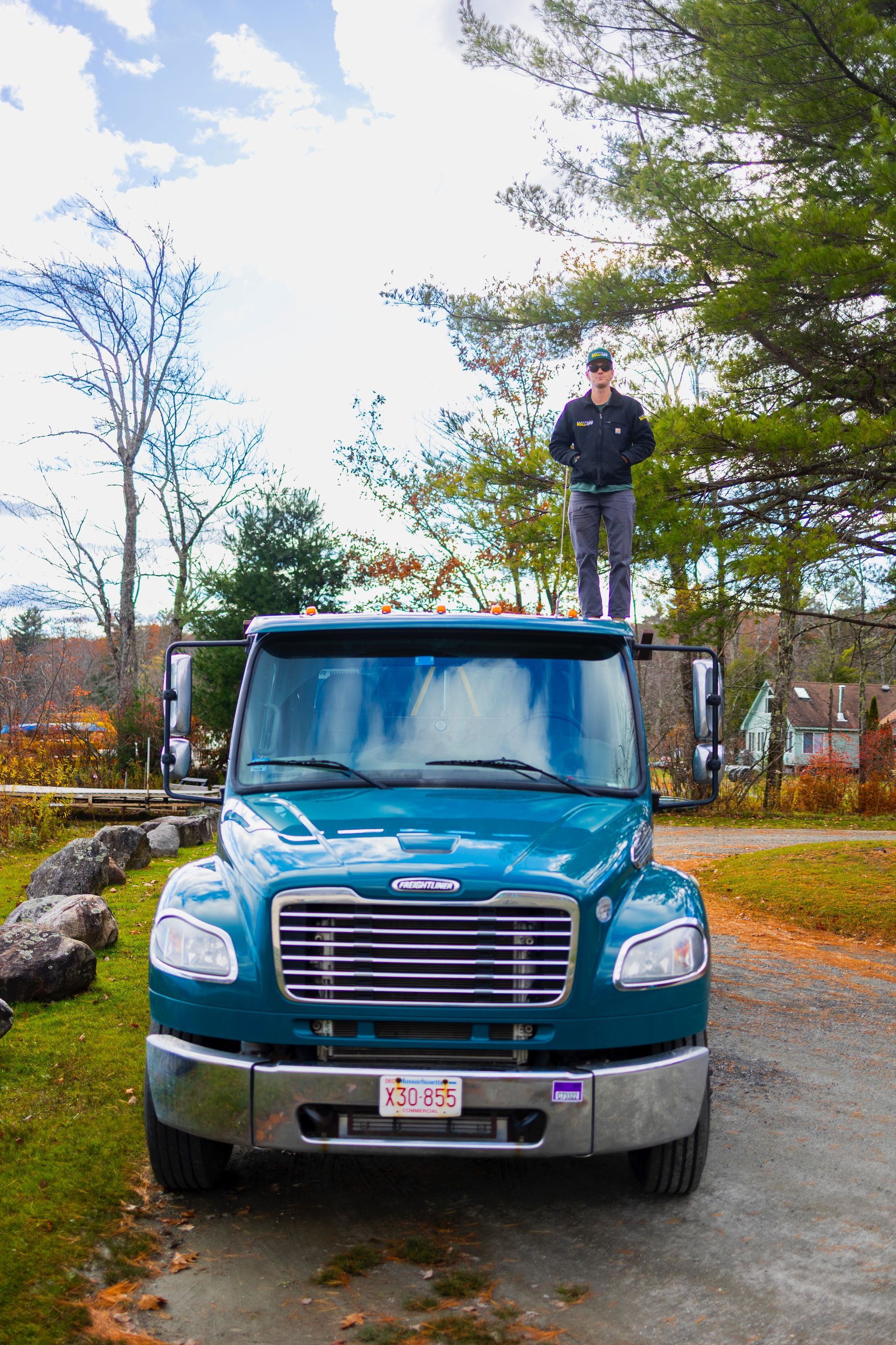Person standing on top of a blue truck on a tree-lined street in autumn