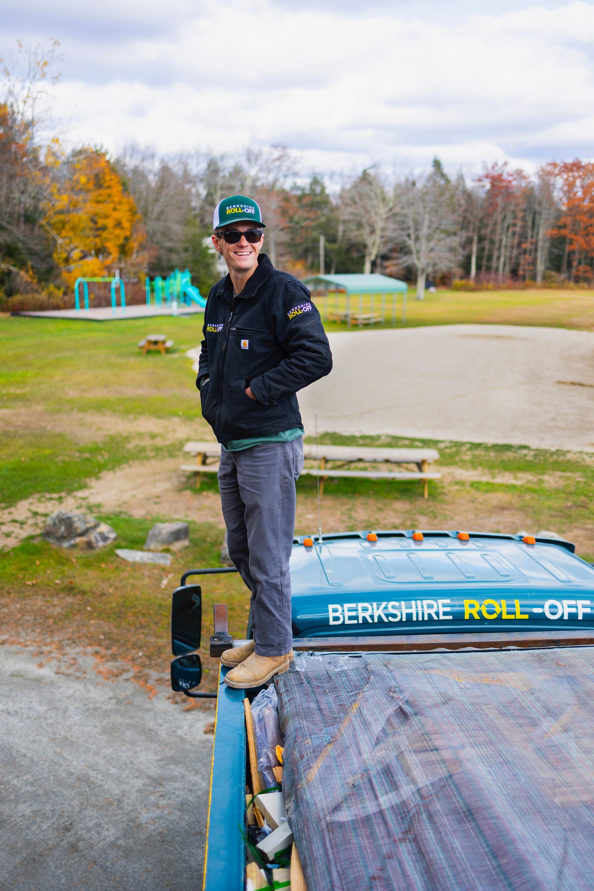 Person standing on a ski lift platform beside a snowboard in an outdoor park, wearing a helmet and sunglasses