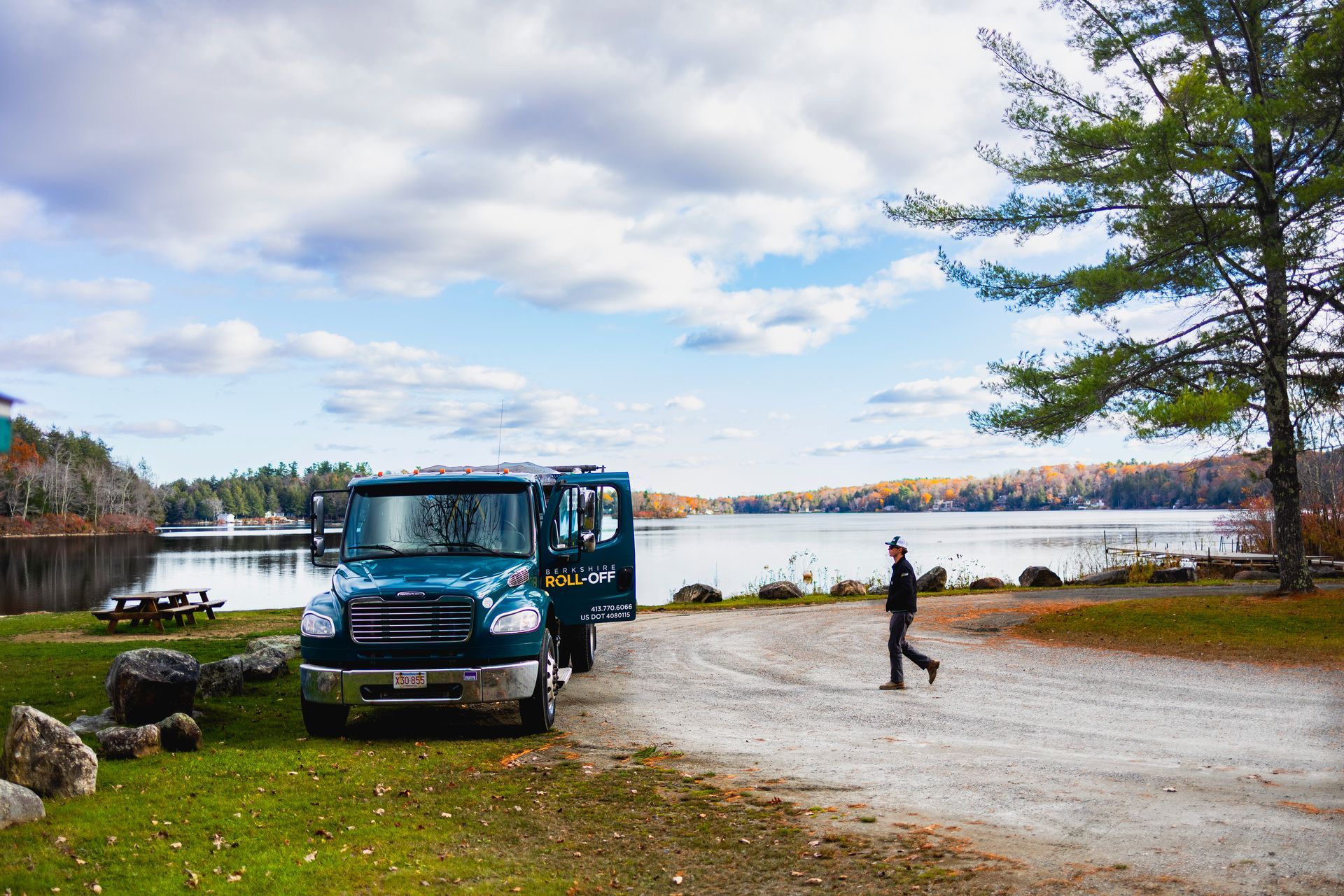 Blue truck parked by a lakeside road under cloudy sky, with a person walking nearby.