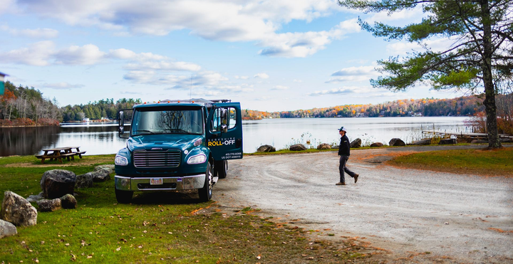 Blue van parked by a lakeside with a person walking on a gravel shore under a partly cloudy sky