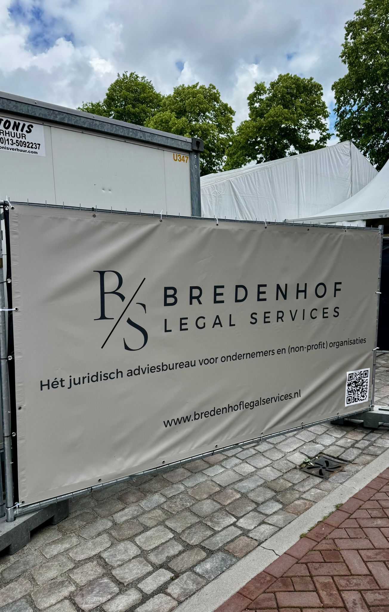 Bord van Bredenhof Juridische Diensten: grijze banner met zwarte tekst, bevestigd aan metalen hekwerk.