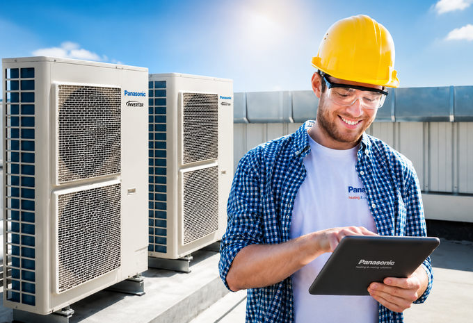 Tecnico con elmetto giallo che controlla le unità HVAC sul tetto con un tablet