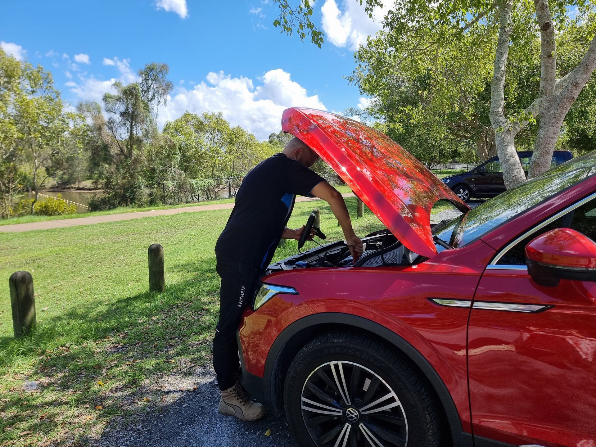 A Person in Dark Clothing Checking the Engine of a Red Car — ASAP Batteries & Breakdowns in Robina, QLD