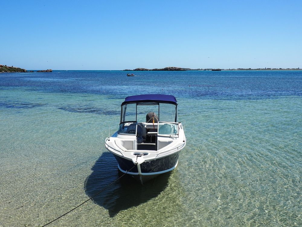 A Small Motorboat With a Blue Canopy Anchored in Clear Turquoise Water — ASAP Batteries & Breakdowns in Southport, QLD