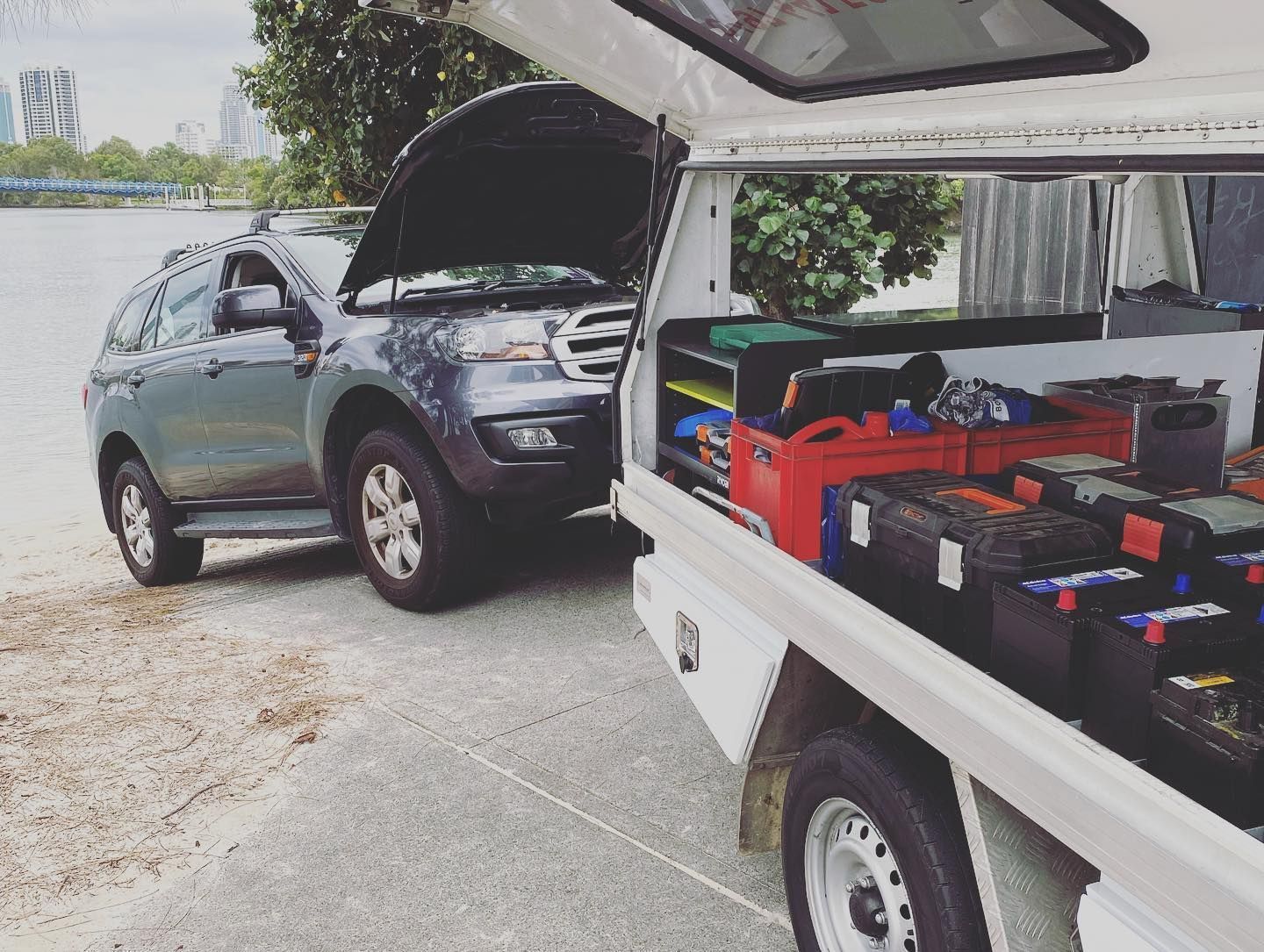 A Dark SUV With Its Hood Up is Parked Near a Water-side Road — ASAP Batteries & Breakdowns in Coomera, QLD