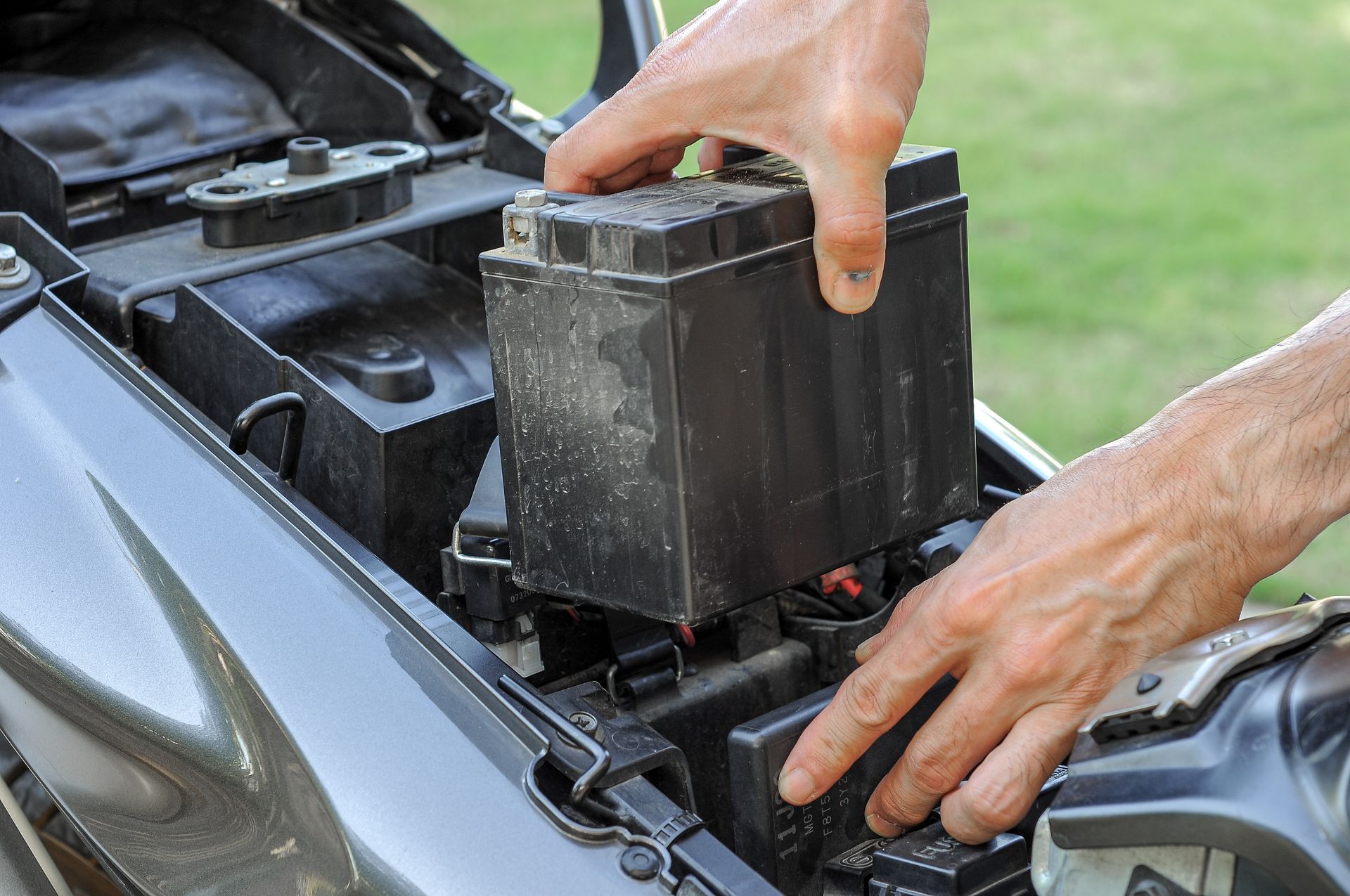Hands Placing a Black Rectangular Motorcycle Battery — ASAP Batteries & Breakdowns in Southport, QLD