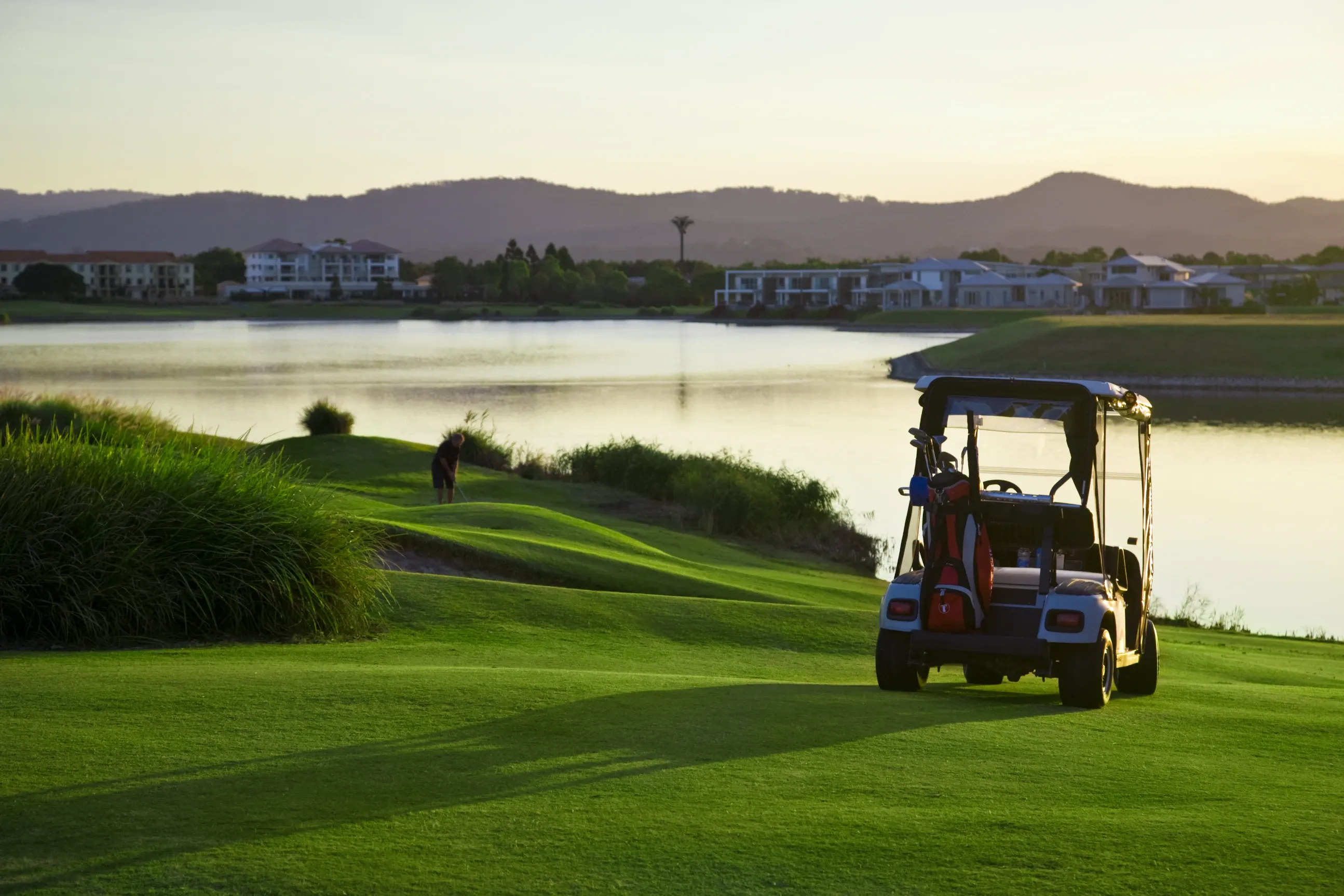 Golf cart on a green overlooking a lake and houses at sunset. — ASAP Batteries & Breakdowns in Burleigh Heads, QLD