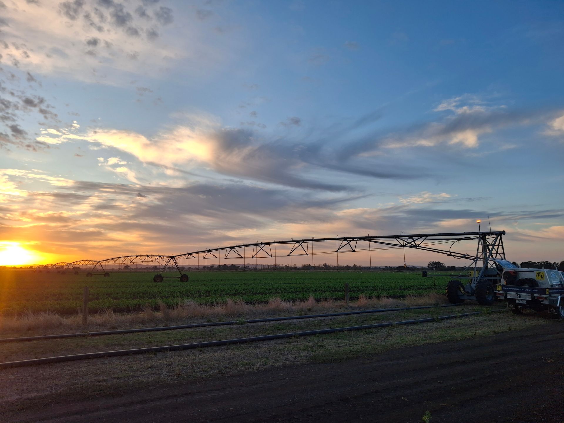 Center-pivot irrigation watering green crops in a field at sunset