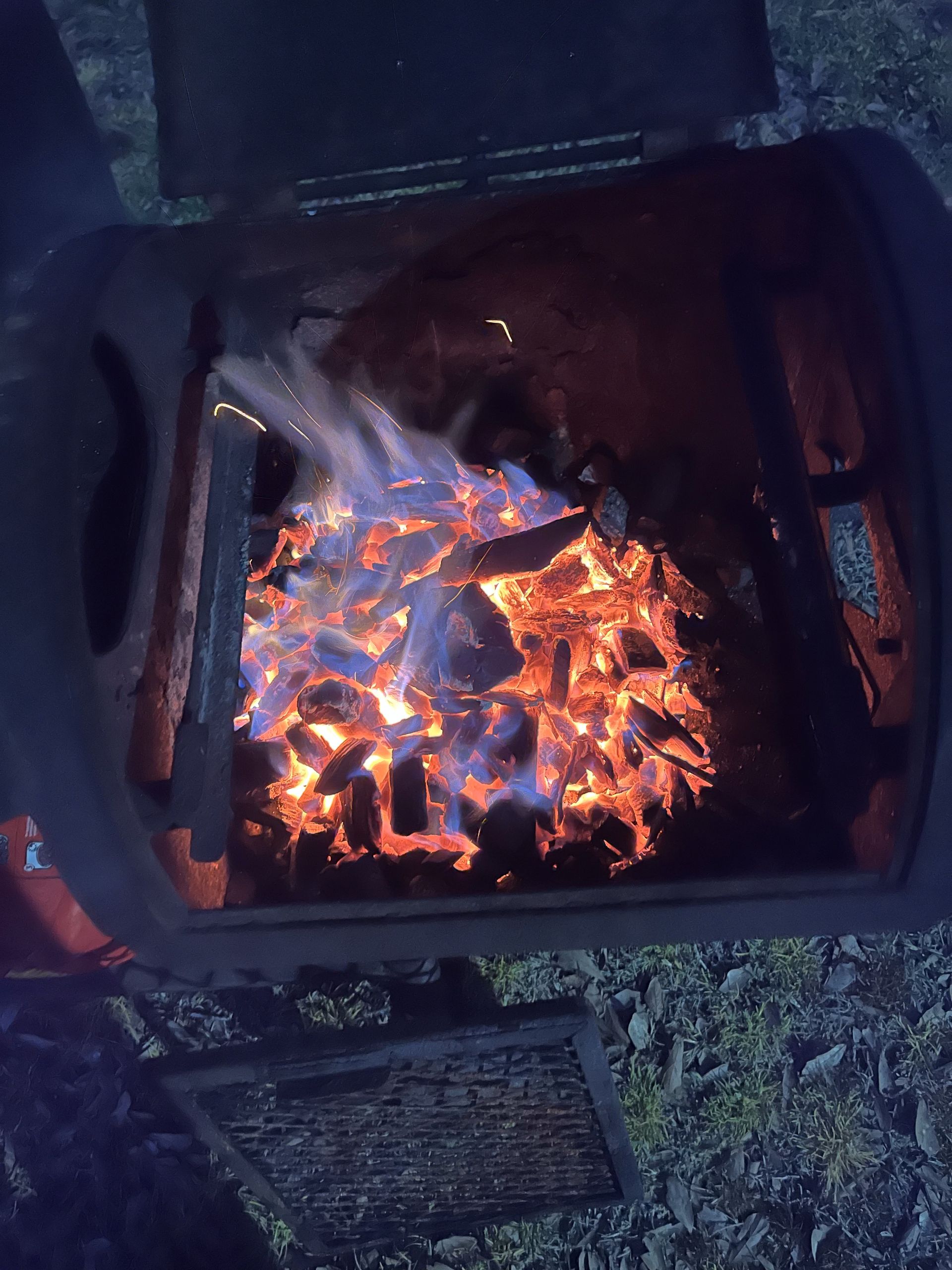 Glowing charcoal embers and small flames burning in a dark metal grill.