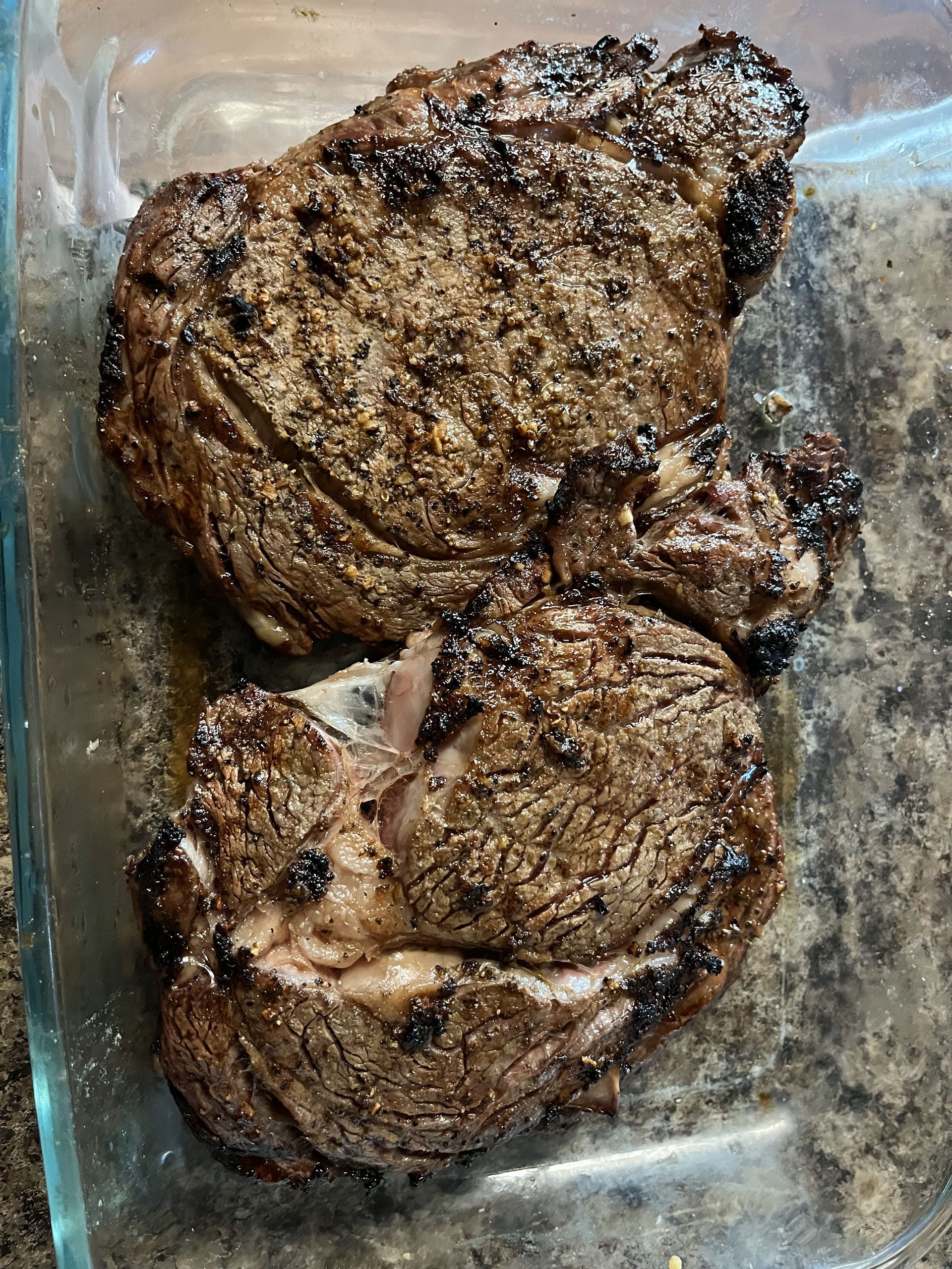 Two steaks are sitting in a glass dish on a table.