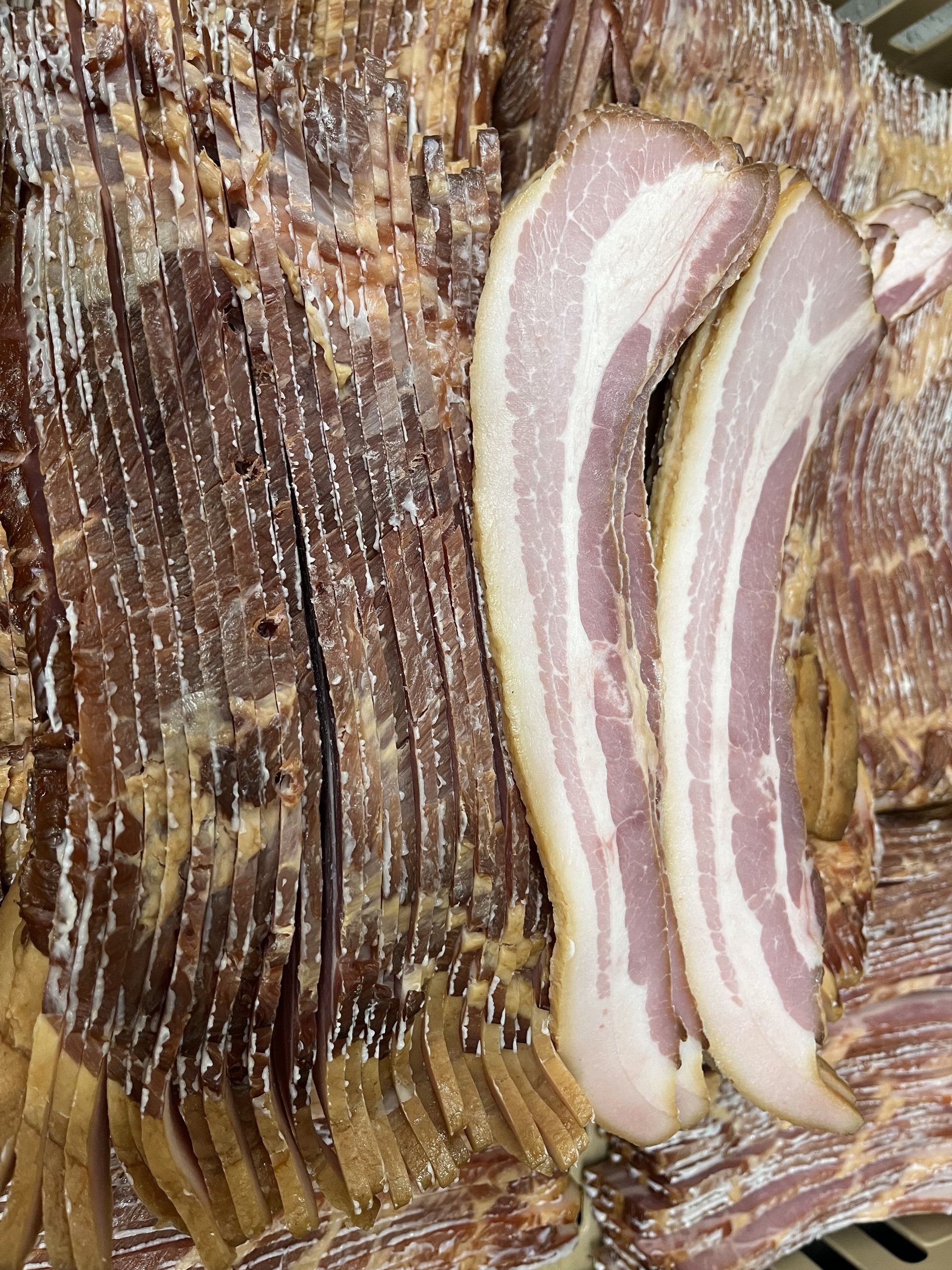 A close up of a piece of bacon sitting on top of a pile of bacon.