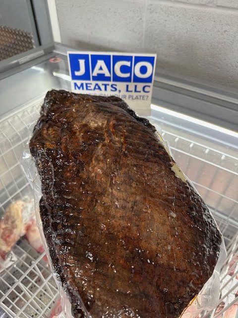 A large vacuum-sealed smoked brisket sits in a display freezer in front of a blue and white Jaco Meats, LLC sign.
