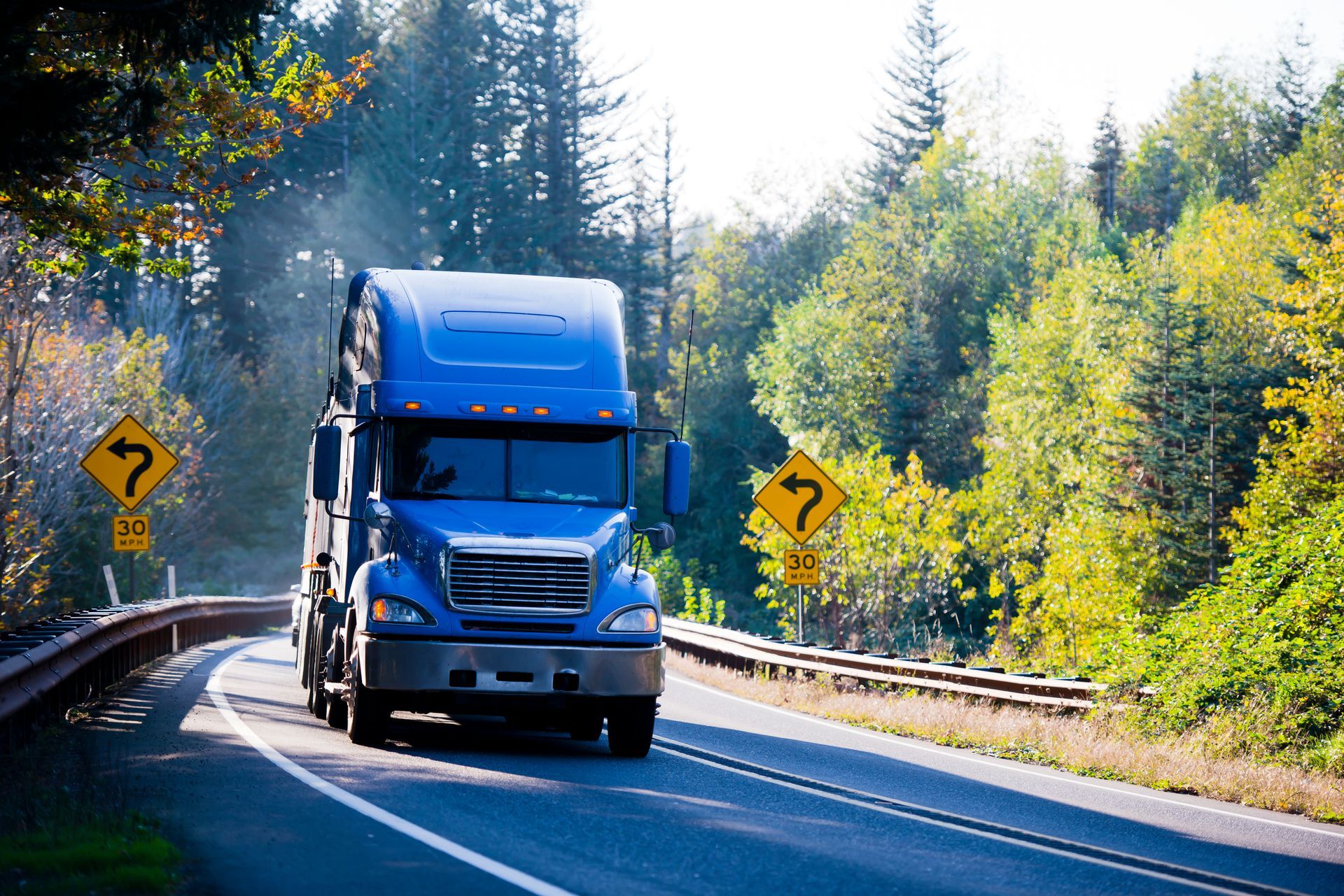 Un semi-remorque bleu roule sur une autoroute sinueuse.