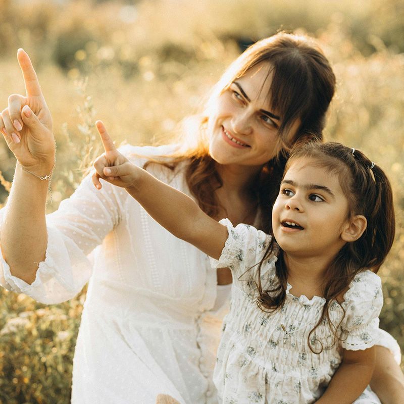 Woman and child pointing upward in a sunlit field, smiling and looking at something off-camera