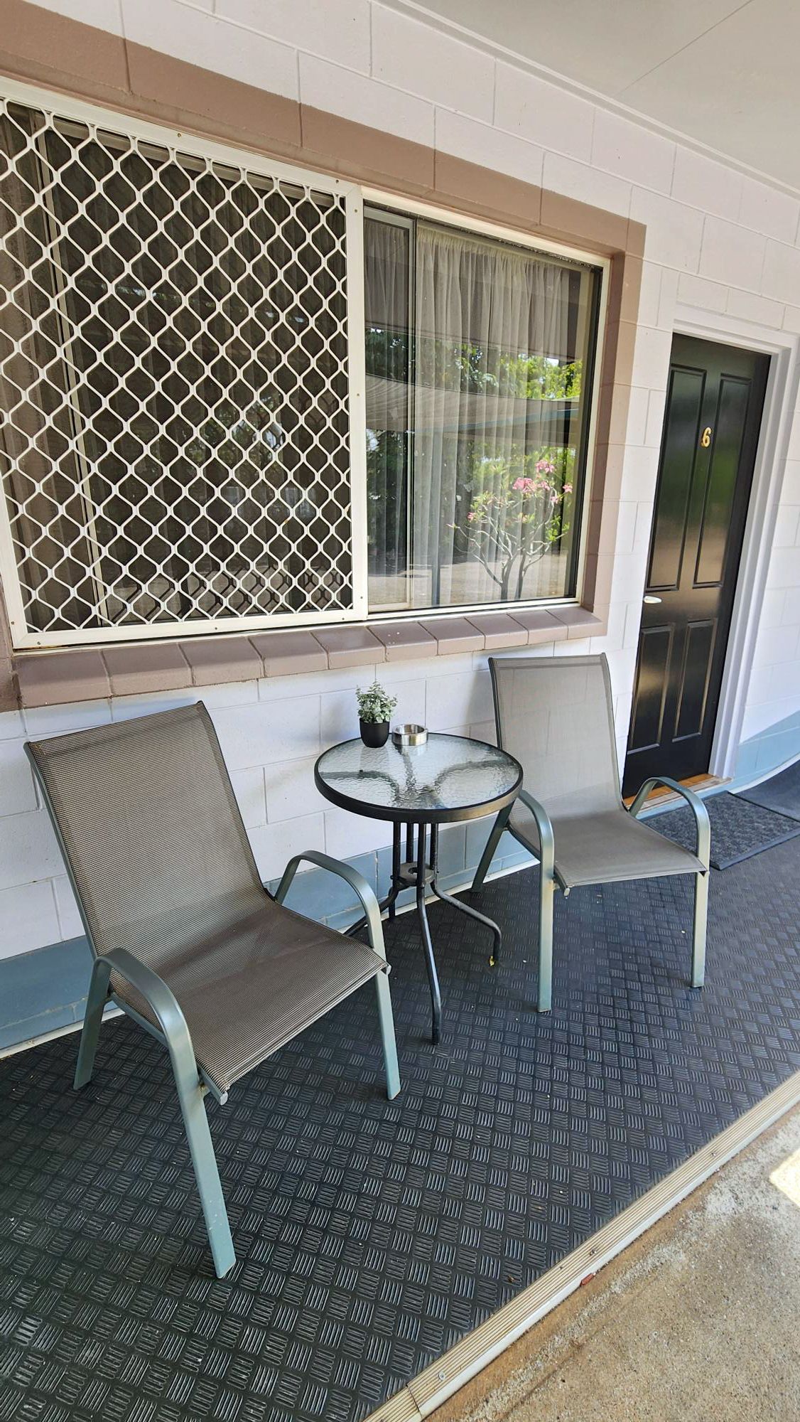 Small porch with two chairs and a glass-top table beneath a window and security screen.