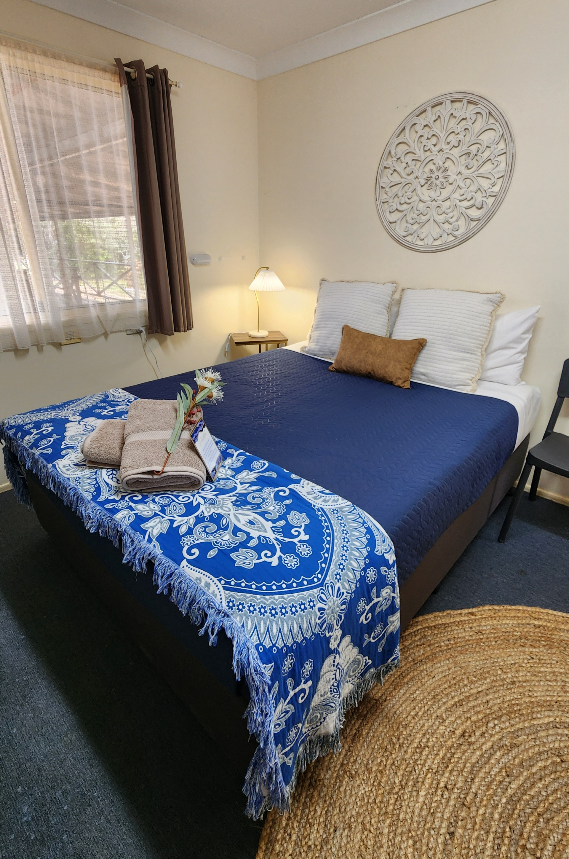 Cozy bedroom with a blue bedspread, lamp, window curtains, wall decor, and woven rug