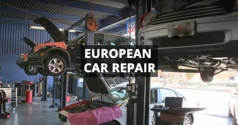 A car is being repaired in a garage with the hood open.