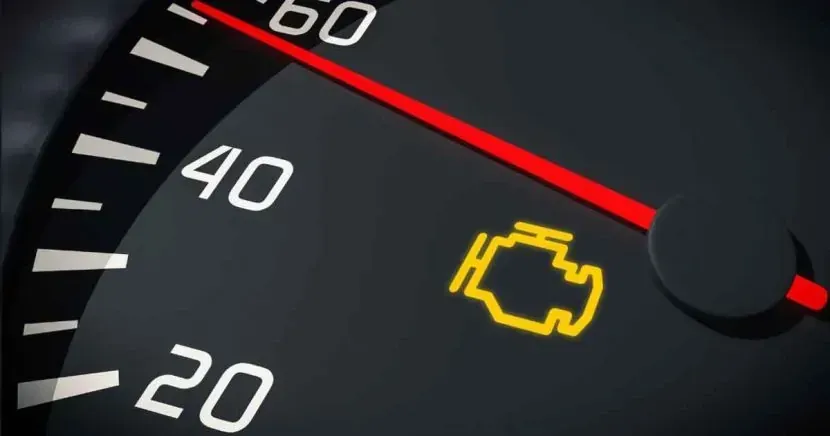 A close up of a speedometer with a yellow engine light on it