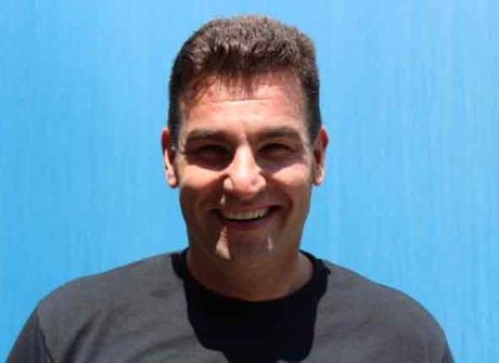 A man in a black shirt is smiling in front of a blue wall.