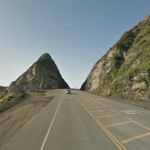A car is driving down a highway between two mountains.