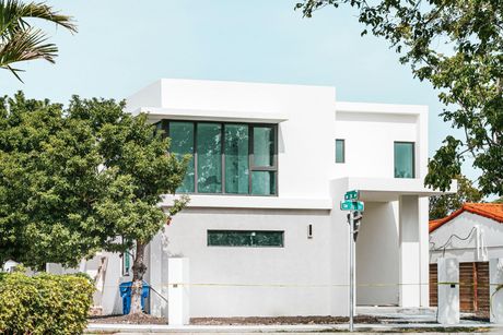 Modern white two-story house with large green-tinted windows and trees in front