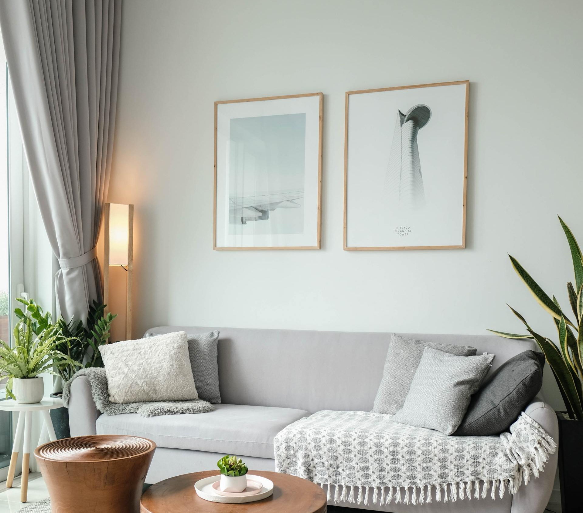 Bright modern living room with a gray sofa, wall art, plants, and a wooden coffee table