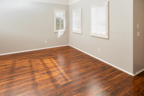 Empty room with hardwood floors, light gray walls, and three windows with blinds.