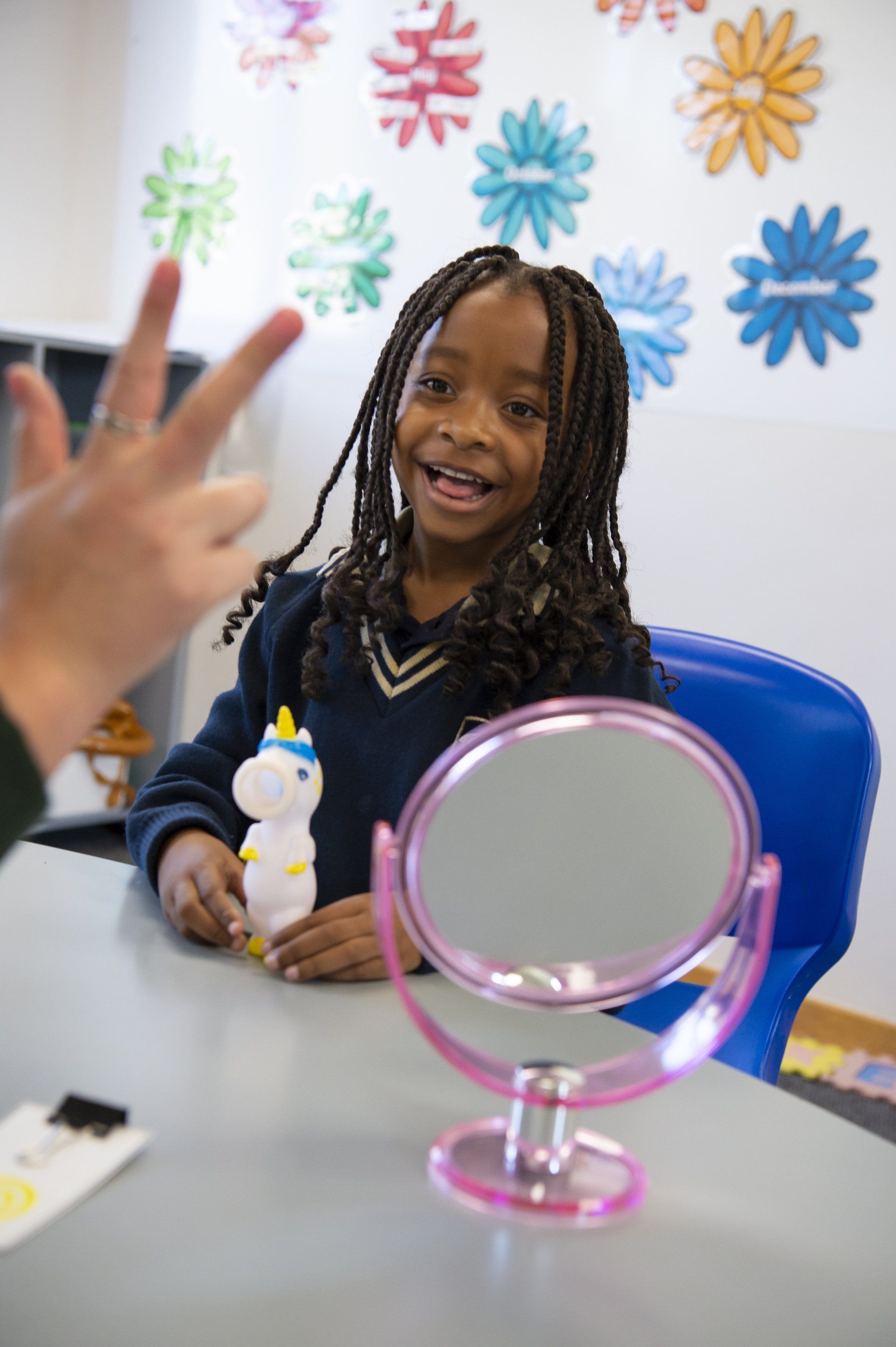 A little girl is sitting at a table looking at herself in a mirror.