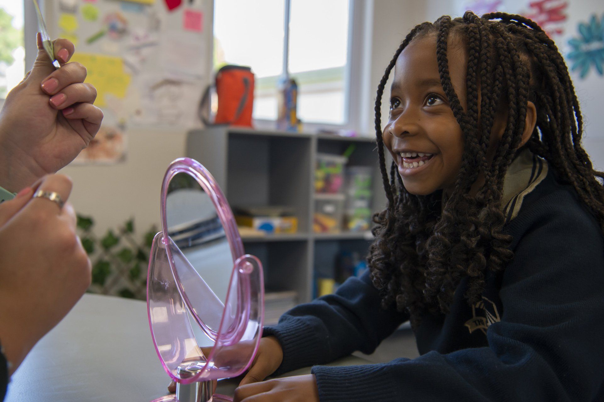 A young girl is sitting at a table looking at herself in a mirror.