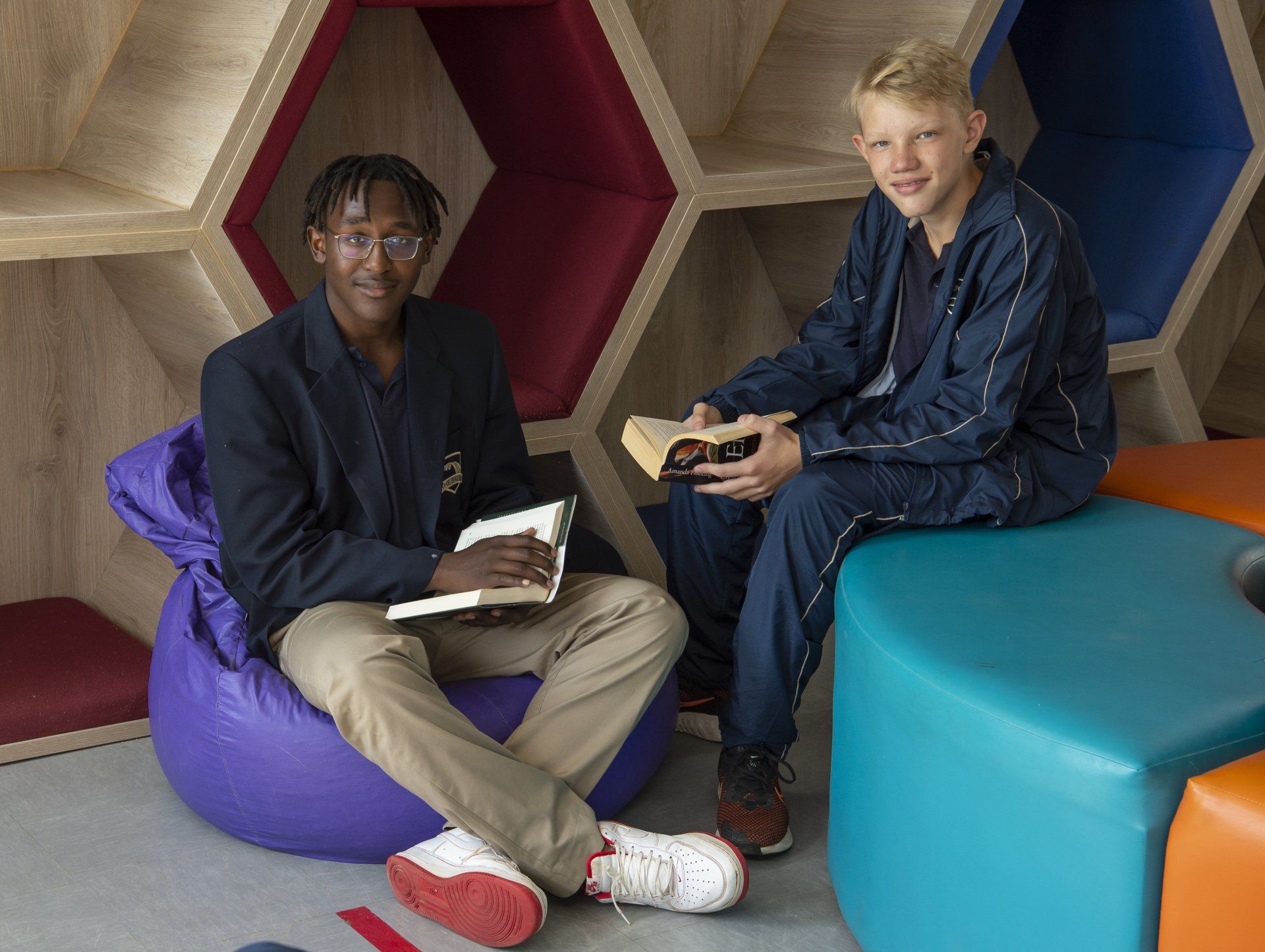 Two young men are sitting on bean bags holding books.