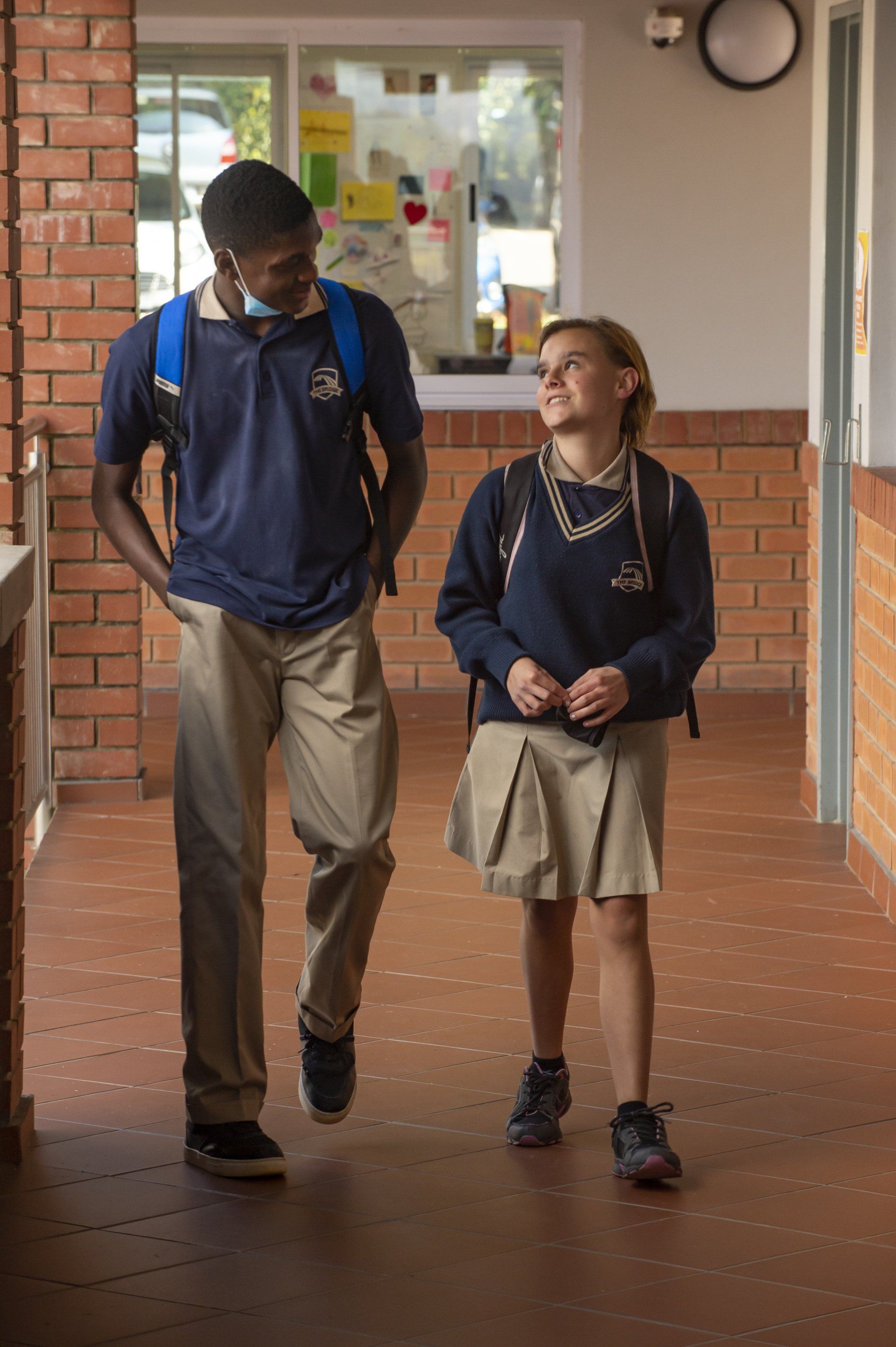 a boy and a girl are walking down a hallway .