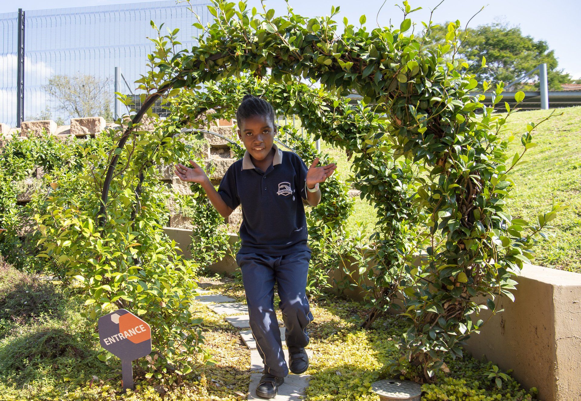 A young boy is walking through a green archway.