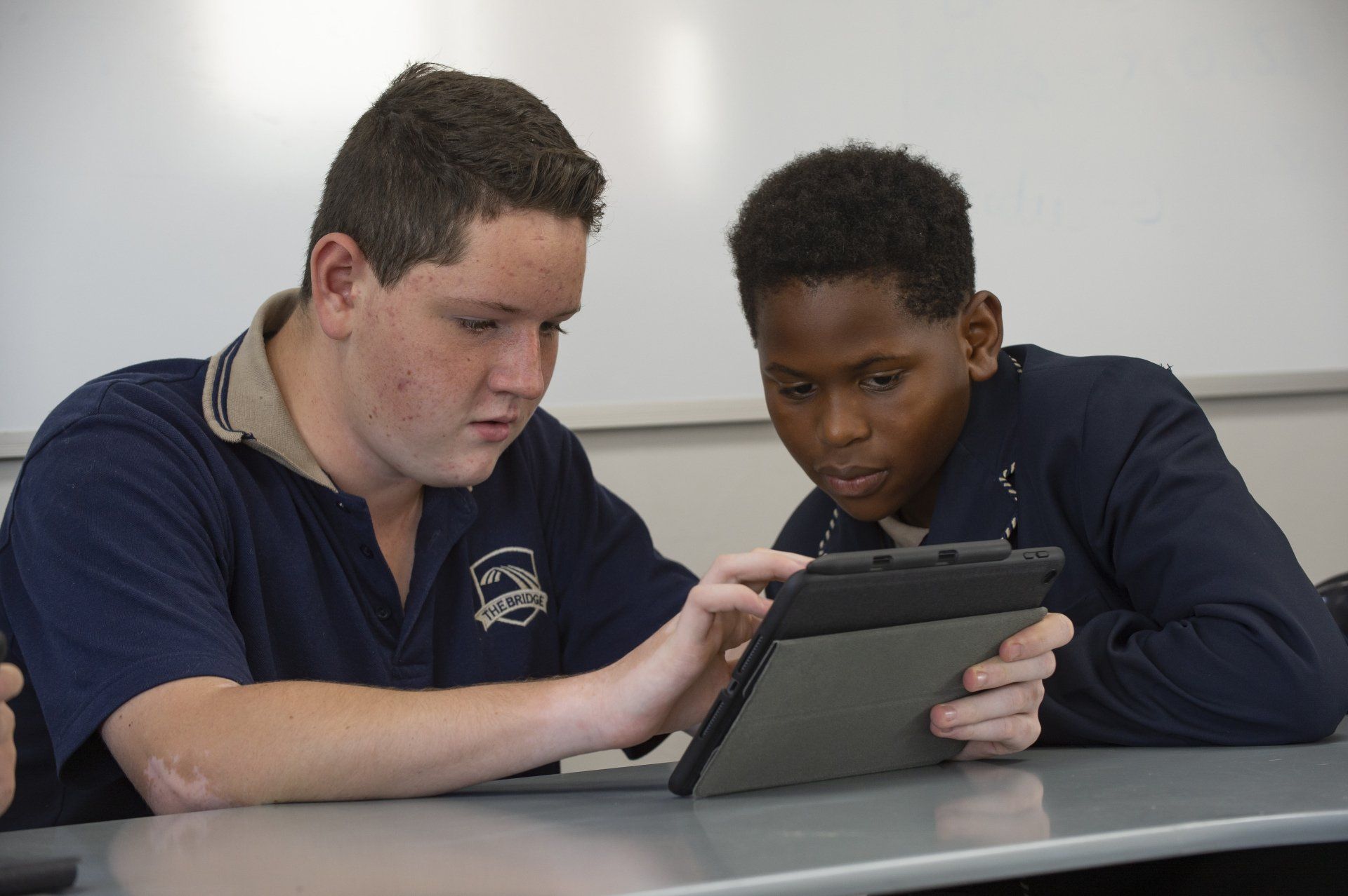 Two boys are looking at a tablet together in a classroom.