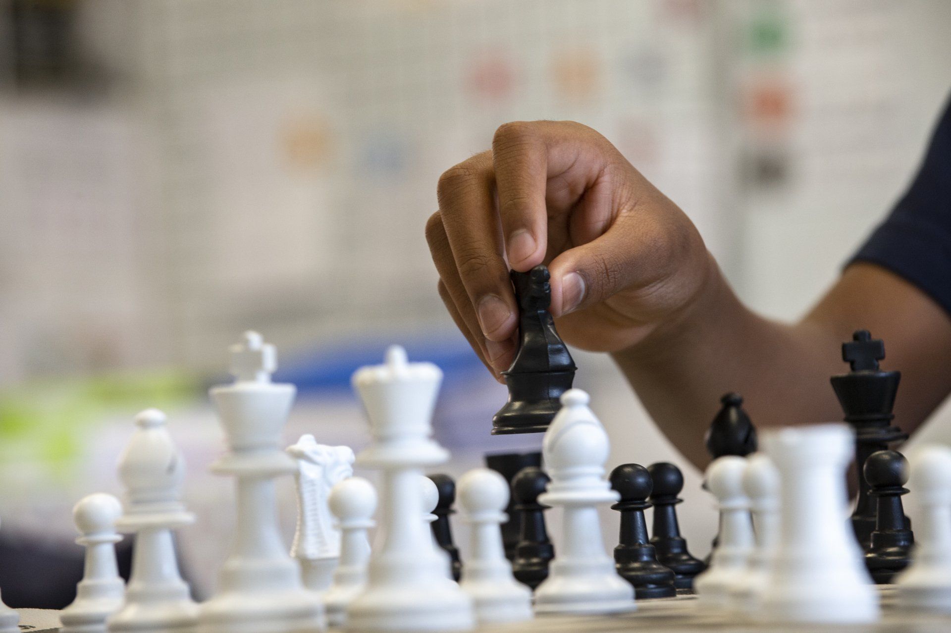 A person's hand moves a black chess piece on a chessboard.