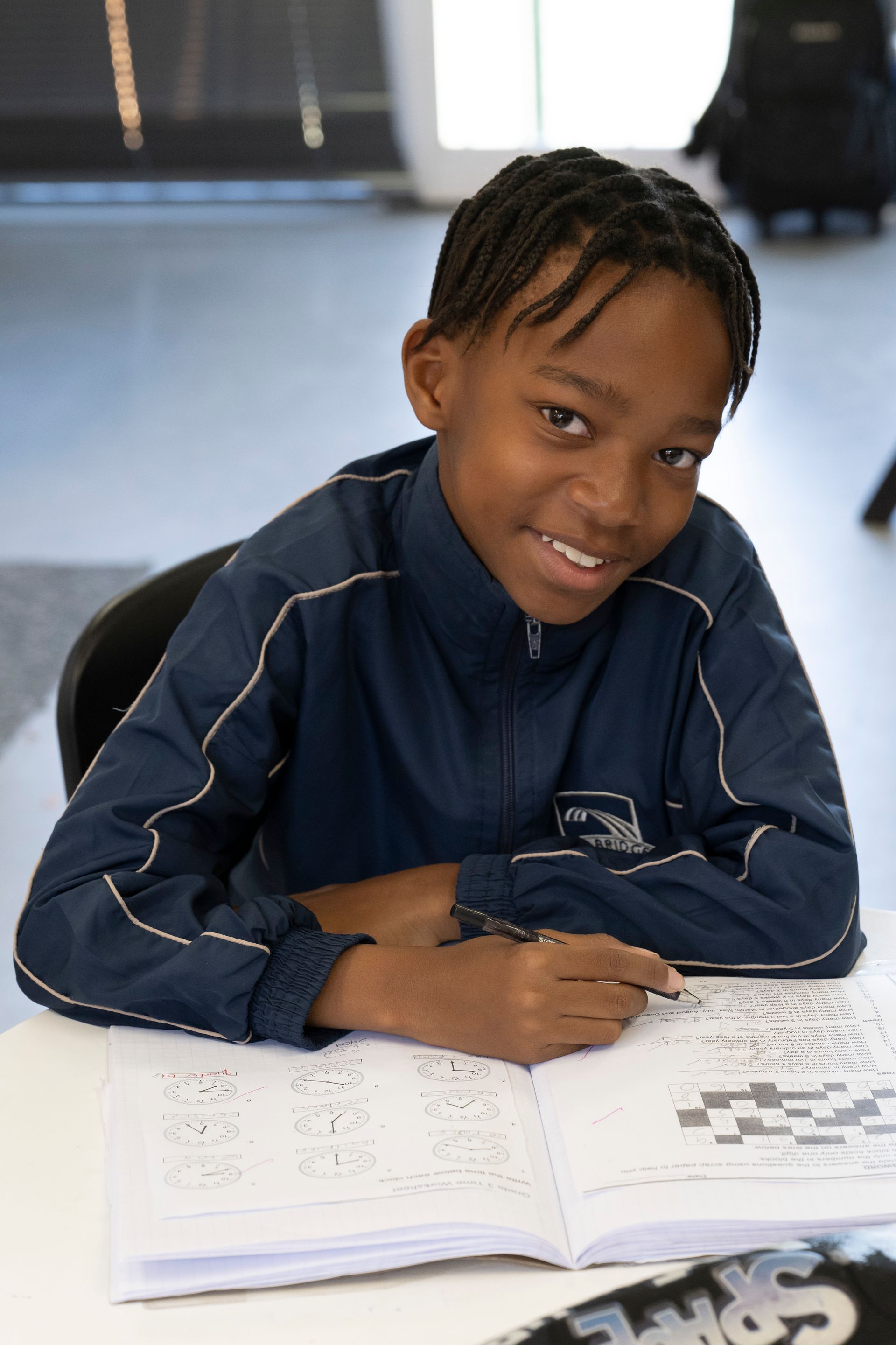 Young Black boy smiles while working on a crossword puzzle in a classroom setting.