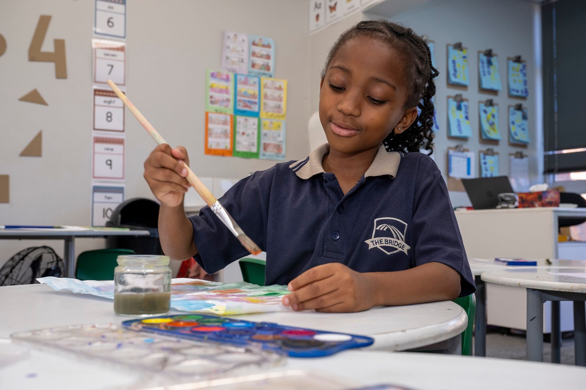 Girl in school uniform paints with watercolor paints in a classroom.