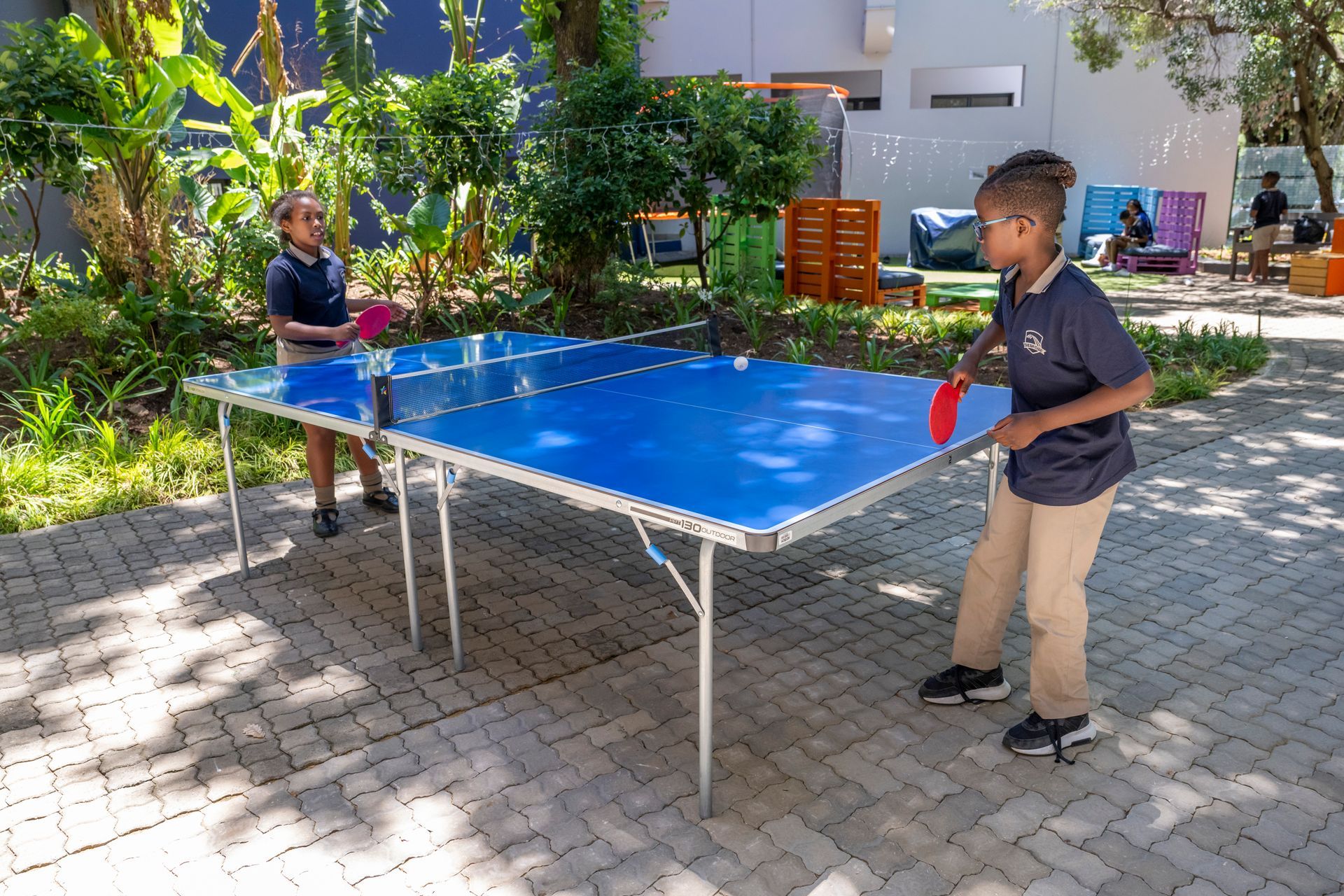 Two children playing table tennis outdoors.