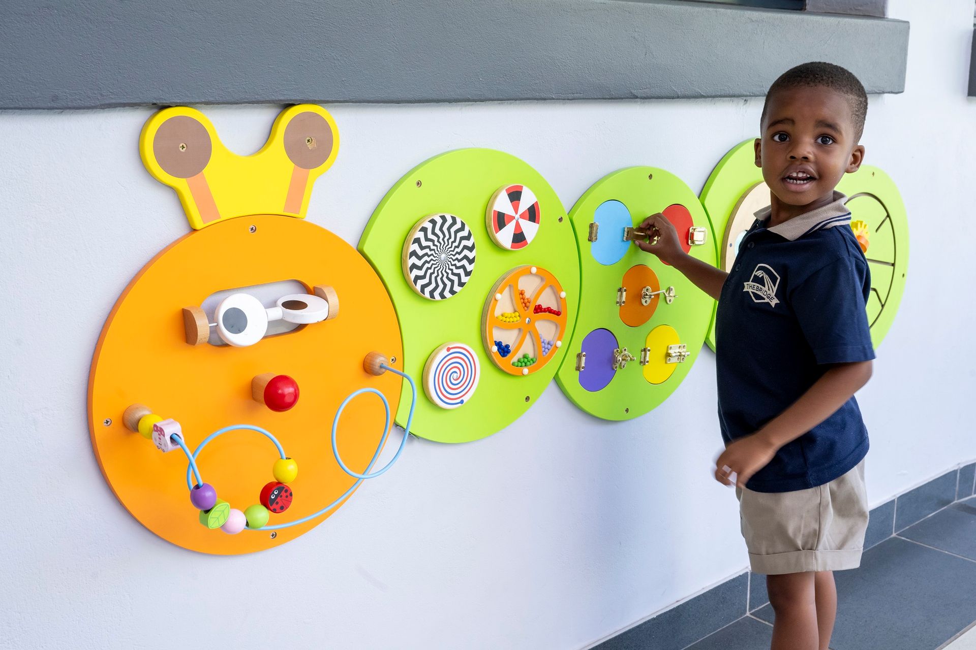 Young child playing with colorful educational wall panel.