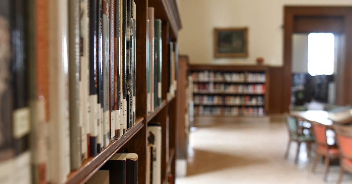 Bookshelves in a library; books in focus, background with more books, a doorway, and chairs.