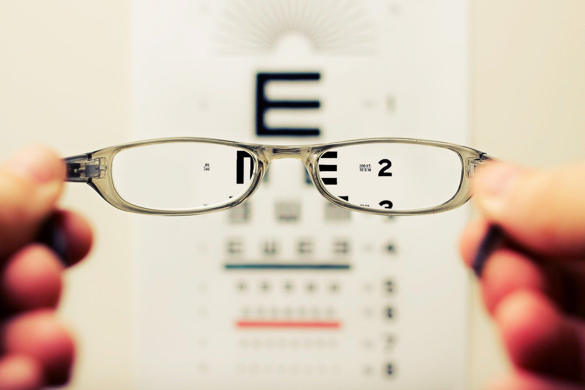 A person is holding a pair of glasses in front of an eye chart
