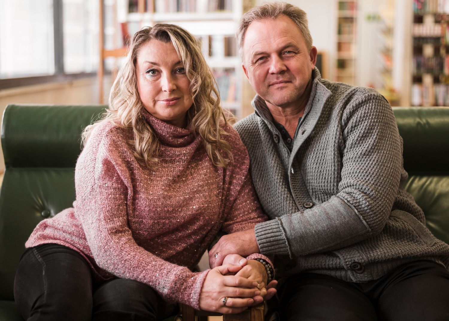 Two people sitting closely on a couch, holding hands and smiling in a cozy living room