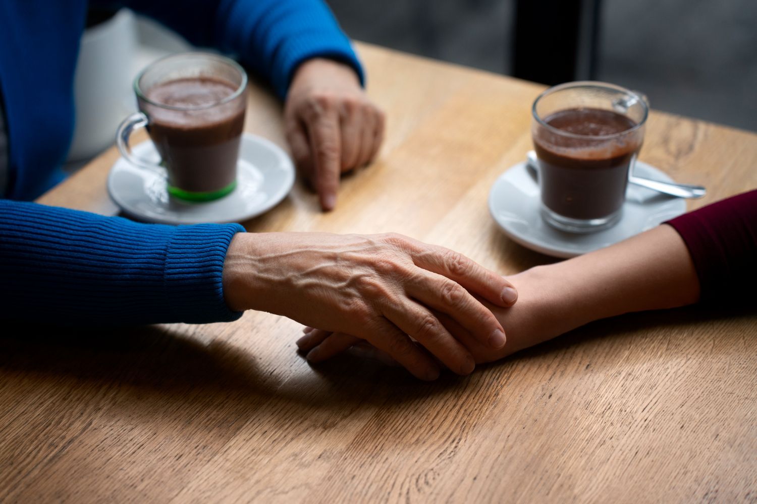 Two people holding hands at a wooden table with two cups of tea in the background
