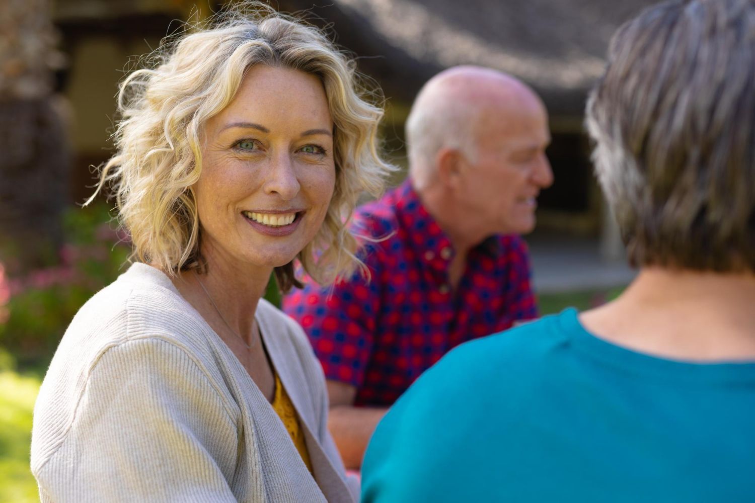 Smiling woman in a light sweater outdoors, with two people seated behind her.