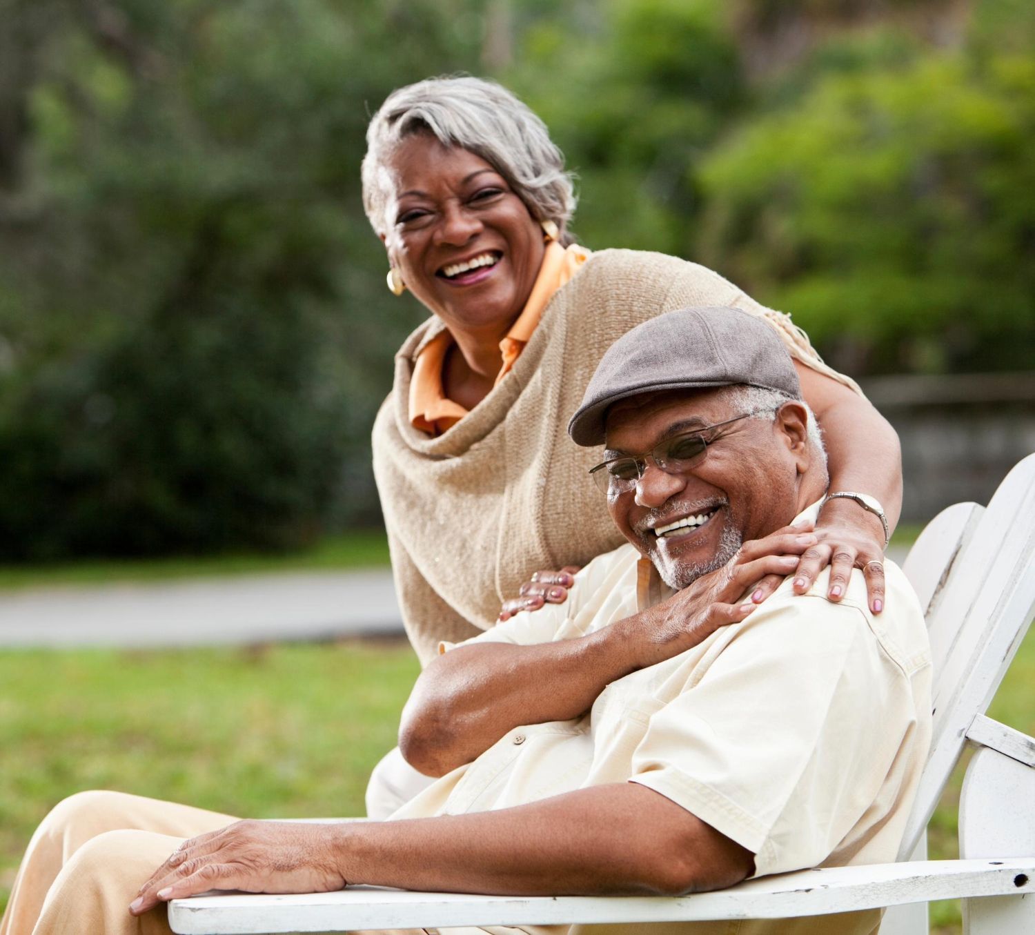 Smiling couple sitting on a white bench in a park, one leaning affectionately on the other.