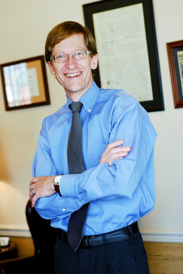 Smiling man in a blue shirt and tie standing with arms crossed in an office setting
