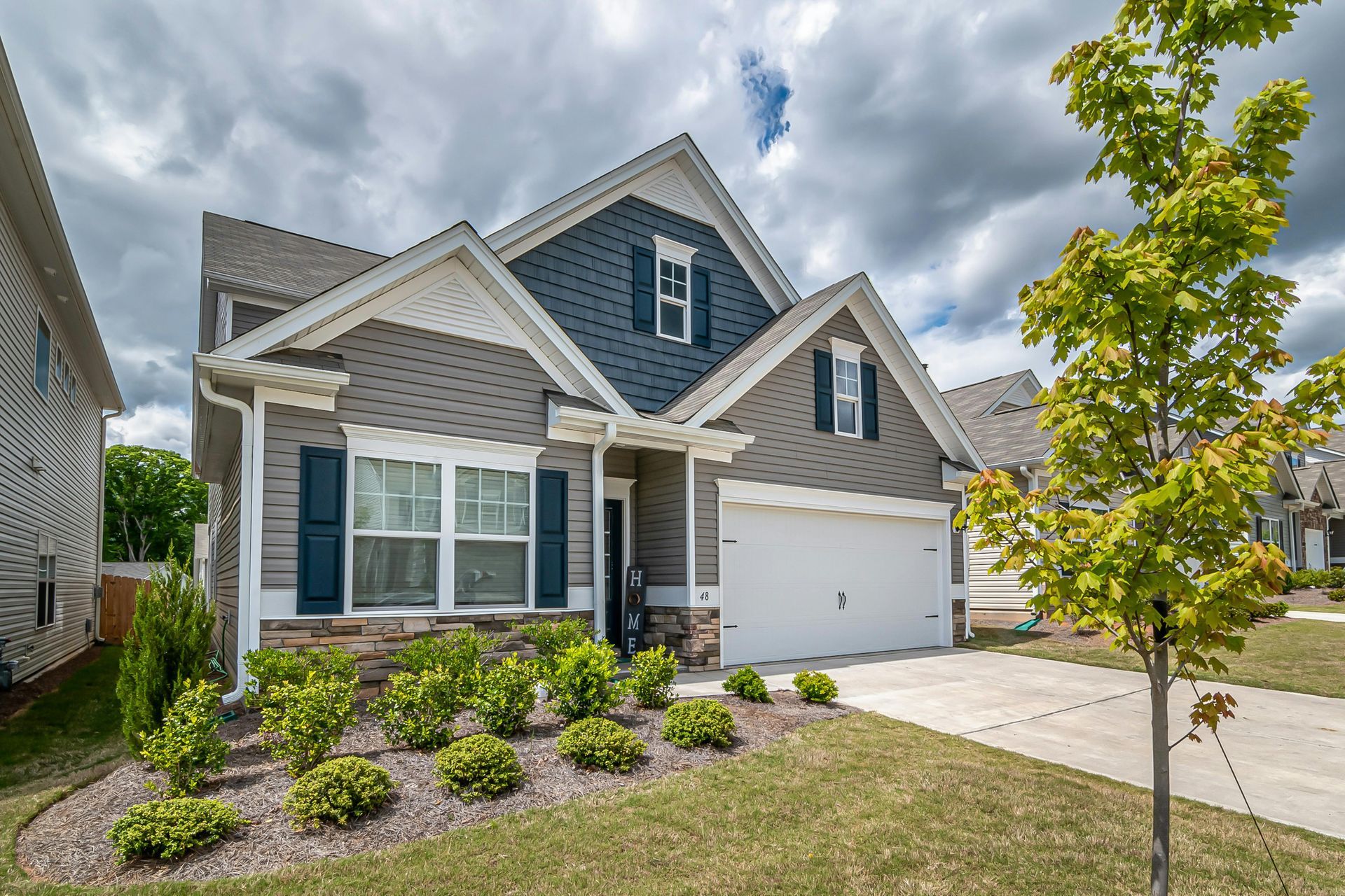 New gray suburban house with white trim, front porch, landscaped yard, and two-car garage