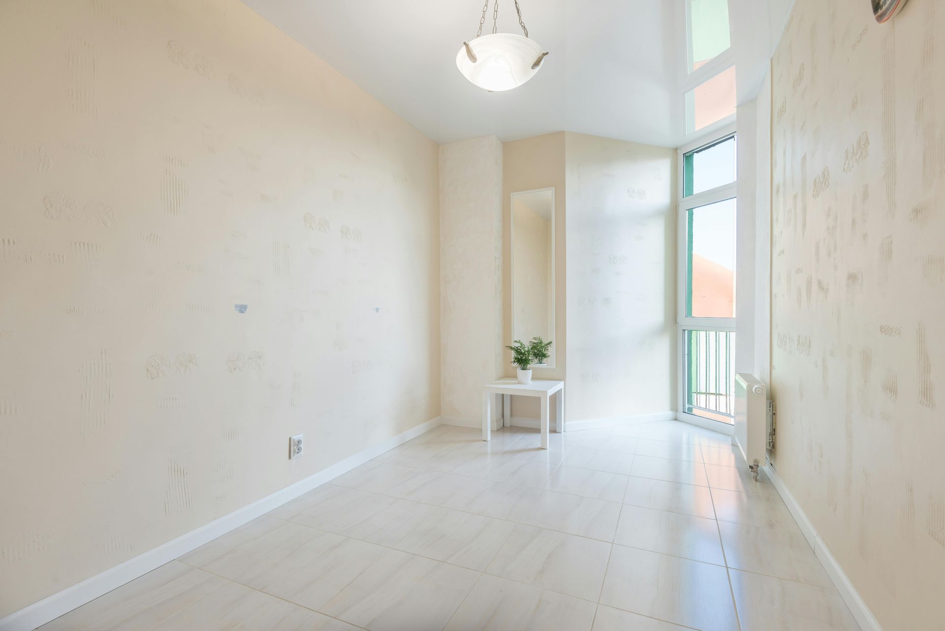 Bright empty white room with light wood floors, tall window, and a small plant on a table