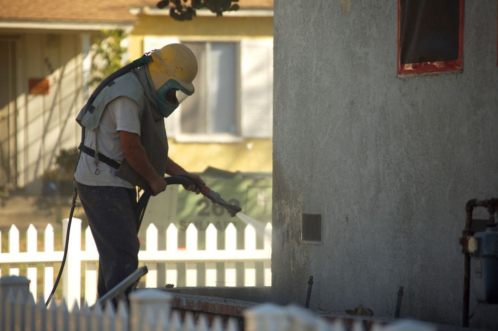 Worker spraying a house wall with a hose in a shaded yard