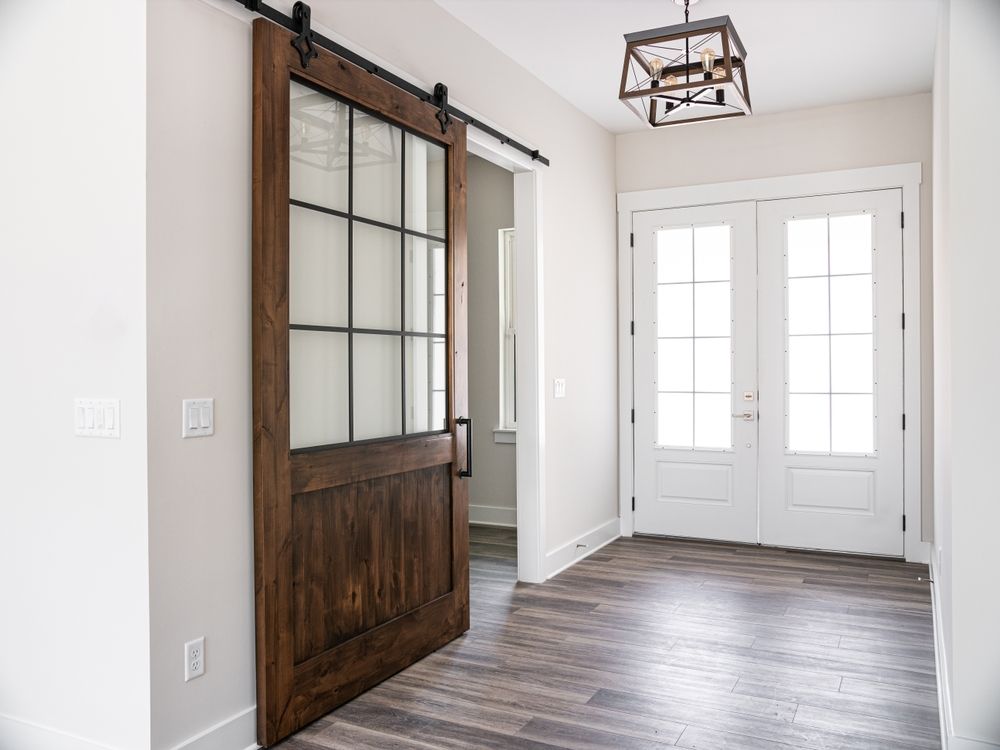 Modern entryway with sliding barn door, white French doors, gray wood floor, and black lantern light fixture