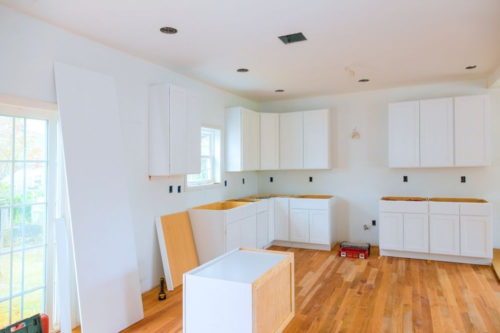 Bright white kitchen under renovation with cabinets, counters, and wood floors